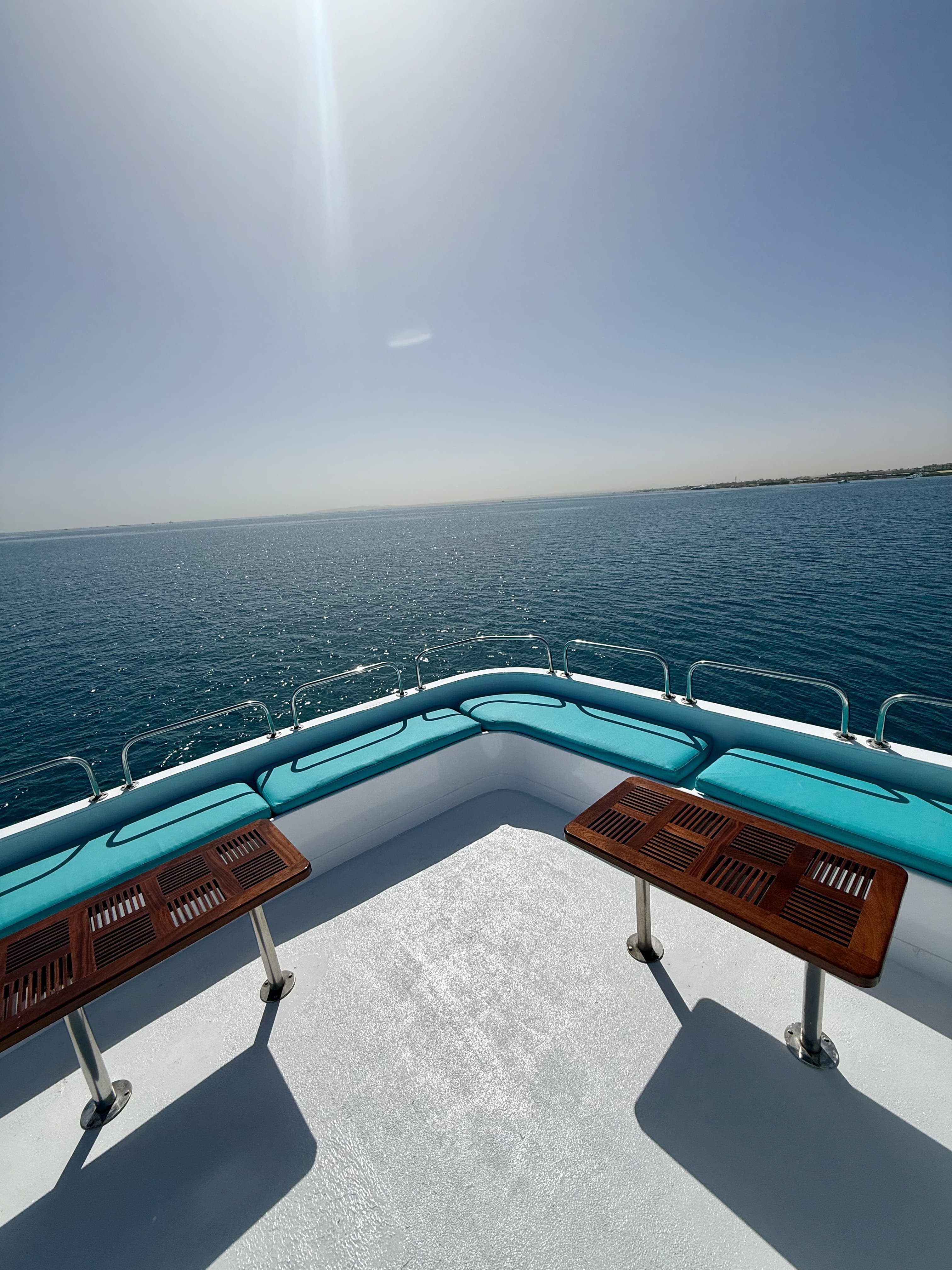Bow sun deck with turquoise cushioned benches and teak tables overlooking the Red Sea